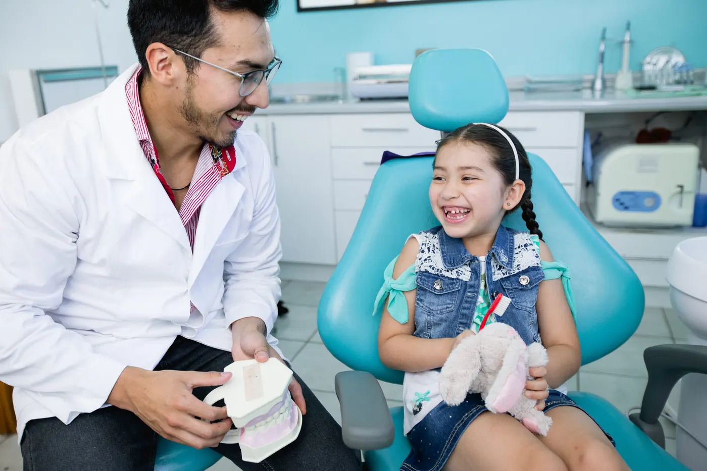Niña sonriendo en un sillón dental junto a su dentista.
