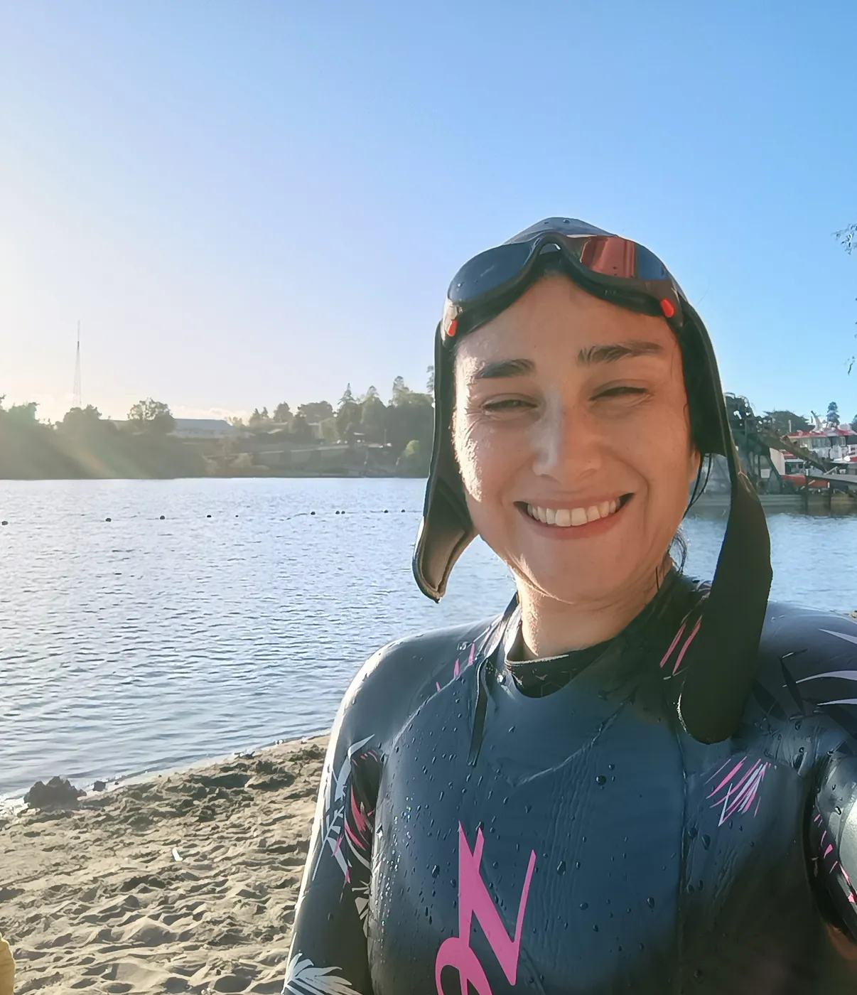 Isabel sonriendo con traje de neopreno, gorro y antiparras a la orilla de un río, después de nadar.